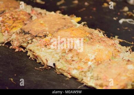 Famoso Japanese street food chiamato Okonomiyaki essendo disposti in corrispondenza di banchi di cibo a Tokyo Foto Stock