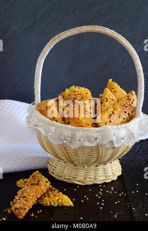 Biscotti salati con semi di sesamo in un cesto su un astratto sfondo grigio Foto Stock