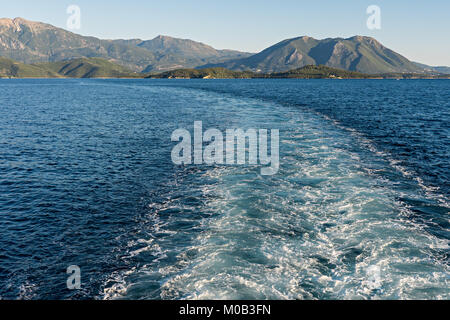 Sentiero sulla superficie del mare dietro una nave con le montagne in distanza Foto Stock