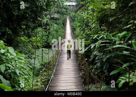 Giovane ragazzo occidentale attraversando ponte sospeso in Gunung Leuser National Park di Tangkahan, Sumatra, Indonesia Foto Stock