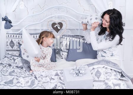 Funny mamma e figlia piccola lotta con cuscini di seduta sul letto in pigiama Foto Stock