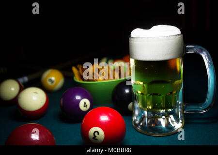 Un freddo boccale di birra su di un verde tavolo da biliardo intorno un sacco di palle da biliardo Foto Stock