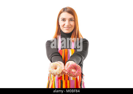 Un rosso giovane dai capelli donna in nero e turtleneck Grembiule da cucina ride e mostra che cosa un fresco ciambelle al cioccolato si è rivelata su un bianco backgrou isolato Foto Stock