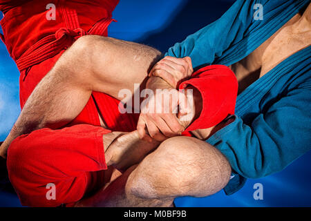 Uomo di lottatori alle prese e jiu jitsu in blu e rosso kimono rende submission wrestling.delle tecniche di combattimento: armbar, armlock Foto Stock