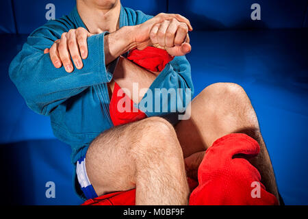 Close-up due lottatori di prese e di jiu jitsu in blu e rosso kimono rende armbar .Submission Wrestling sul tatami blu Foto Stock