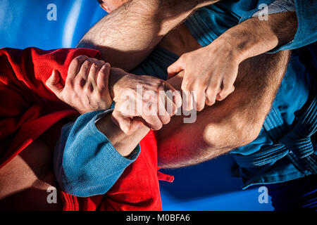 Close-up due lottatori di sambo e jiu jitsu in blu e rosso kimono facendo . L'uomo lottatore rende submission wrestling o armbar sul tatami blu Foto Stock