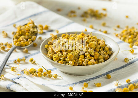 Giallo grezzo organico essiccato il tè camomilla in una ciotola Foto Stock