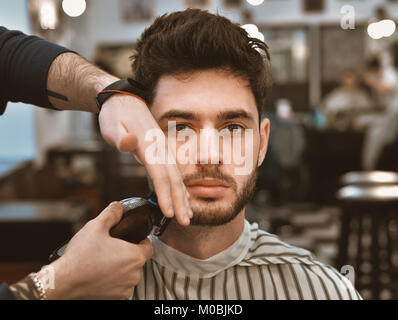 Le mani del giovane barbiere rendendo scarti da uomo attraente in Barberia Foto Stock