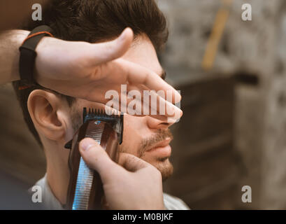 Le mani del giovane barbiere rendendo scarti da uomo attraente in Barberia Foto Stock