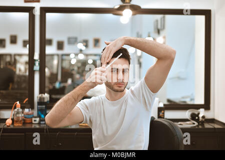 Processo di lavoro in moderno barbiere. Bello il parrucchiere che serve il cliente, per lo styling dei capelli per i maschi di client utilizzando un asciugacapelli. Vista laterale ritratto di attra Foto Stock