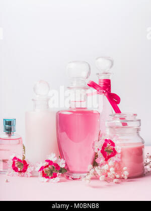 Bellezza e cura della pelle concetto a sfondo luminoso, vista frontale. Vari prodotti cosmetici in bottiglie e vasi con fiori di colore rosa: lozione,profumo, tonico, Foto Stock