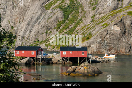 Tipica rorbu cottages in Nusfjord e una barca da pesca la crociera nel mare di Norvegia. Foto Stock