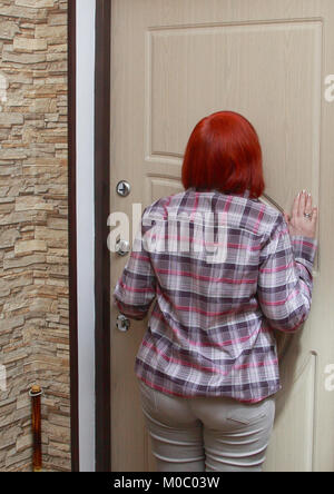 La ragazza chiude la porta dall'interno del suo appartamento. Ella rimane indietro , tenendo la maniglia della porta e si guarda attraverso l'occhio magico. Foto Stock