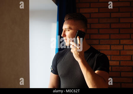 Uomo che parla al telefono in casa vicino alla finestra Foto Stock