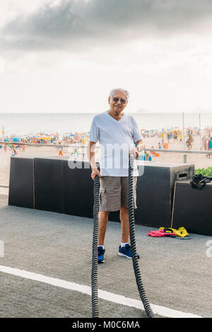 Modello rilasciato: uomo vecchio (80-89) esercitando con combattendo la corda in palestra pubblica a Ipanema, Rio de Janeiro, Brasile Foto Stock