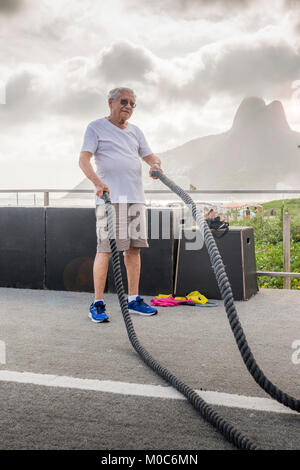 Modello rilasciato: uomo vecchio (80-89) esercitando con combattendo la corda in palestra pubblica a Ipanema, Rio de Janeiro, Brasile Foto Stock