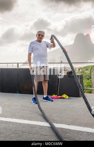 Modello rilasciato: uomo vecchio (80-89) esercitando con combattendo la corda in palestra pubblica a Ipanema, Rio de Janeiro, Brasile Foto Stock