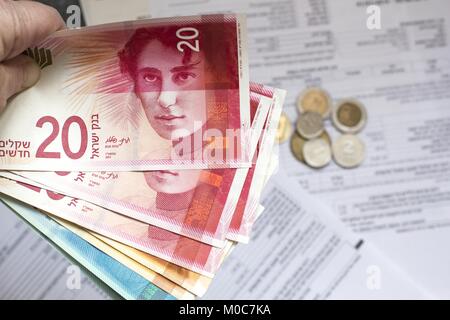 Donna mano che tiene un grappolo di nuovo Israeli Shekel banconote nelle sue mani. Banconote e monete in background Foto Stock