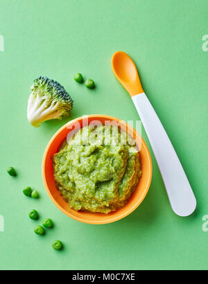 I piselli e i broccoli baby purea in ciotola con cucchiaio bambino su sfondo verde, vista dall'alto Foto Stock