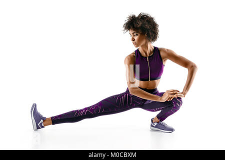 Atleta ragazza il suo allungamento bicipiti femorali. Foto del giovane ragazza africana facendo esercizio su sfondo bianco. Sport Foto Stock