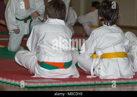 I bambini la schiena girata con il judo bianco uniforme seduto sul Tatami in palestra. Foto Stock