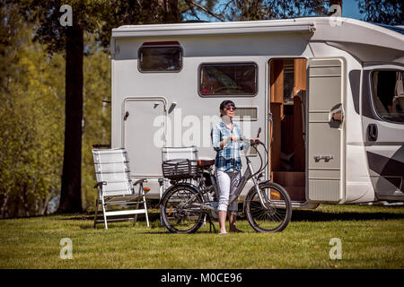 Donna sulla bicicletta elettrica in appoggio al campeggio. Vacanza per la famiglia in viaggio, viaggio vacanza in camper, caravan VR auto vacanza. Foto Stock