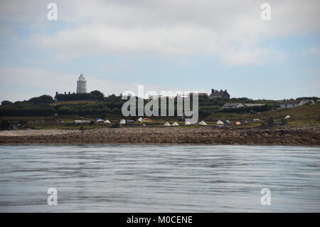 Troy Town Farm Campeggio in Perigus Bay, Città Bassa e il bianco faro in disuso su sant Agnese da Smith Suono, isole Scilly, Cornwall, Regno Unito. Foto Stock