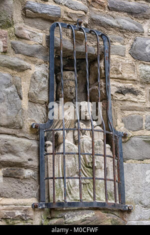 Antico borgo medievale statua di pietra della parete della Vergine Maria con il bambino agli agenti atmosferici lontano dietro le sbarre Foto Stock