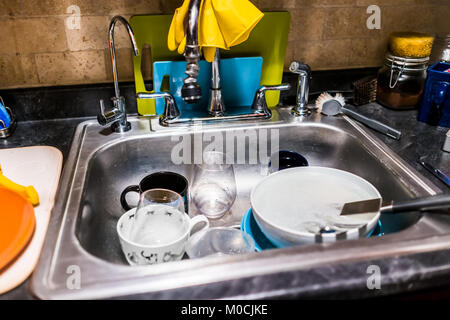 Primo piano dei piatti sporchi nel lavello in acciaio inox cucina per la pulizia di utensili, taglieri, muro di mattoni Foto Stock