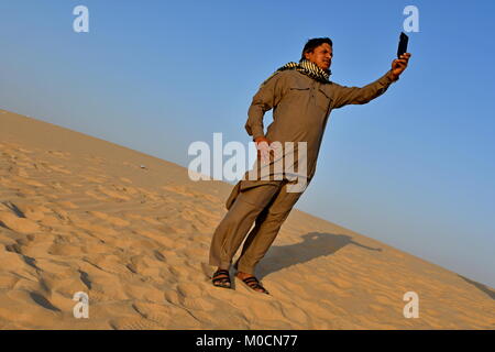 Gli uomini nel deserto di sabbia giocando ed appendere fuori con i telefoni cellulari e rendendo selfies Foto Stock