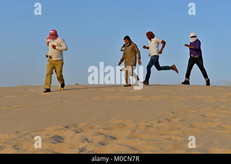 Gli uomini nel deserto di sabbia giocando ed appendere fuori con i telefoni cellulari e rendendo selfies Foto Stock