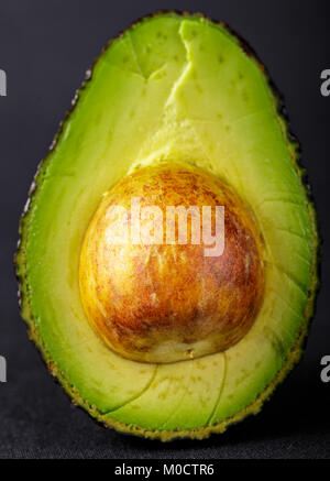 Un avocado maturo scorrono in mezzo con pit seme isolato sul retro nero di massa. Foto Stock