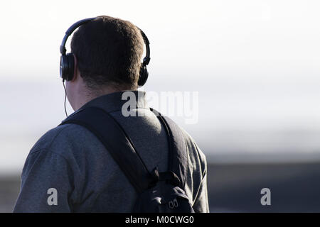 Uomo che indossa le cuffie cablate guardando lontano dalla telecamera. Foto Stock