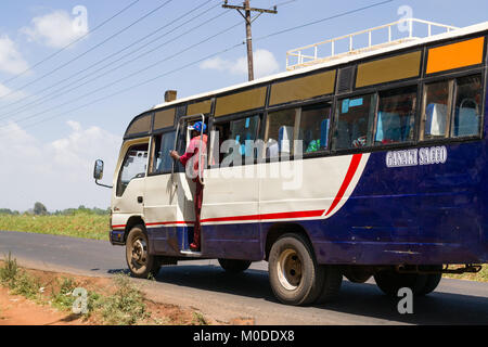 Un bus la guida su una strada con il conduttore in piedi la porta di attesa per i passeggeri, Nairobi, Kenia Foto Stock