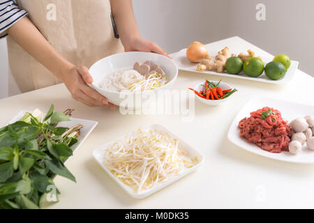 Femmina cuoco preparare la tradizionale zuppa vietnamita Pho bo con erbe aromatiche, carne e riso tagliatelle Foto Stock