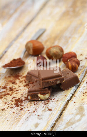 Pezzi di cioccolato croccante con nocciole intere su rustiche superficie in legno Foto Stock