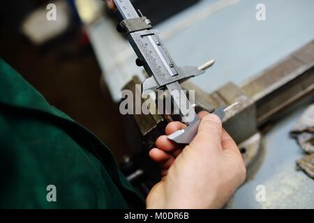 Lavoratore detiene una pinza nelle sue mani e le misure di un dettaglio Foto Stock