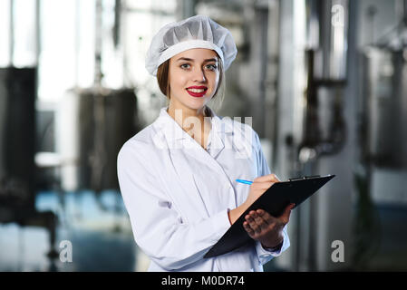 Ragazza carina in bianco vestiti da lavoro rende note su una penna su un tablet Foto Stock