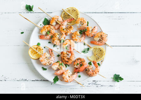 Grigliata di gamberi spiedini. Frutti di mare, shelfish. Gamberi spiedini con spezie e erbe aromatiche fresche in bianco sullo sfondo di legno, copia dello spazio. Gamberi b Foto Stock