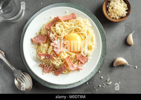 Spaghetti alla carbonara la pasta con la salsa di uova, pancetta e formaggio parmigiano grattugiato - le sane pasta italiana sul cemento grigio sfondo Foto Stock
