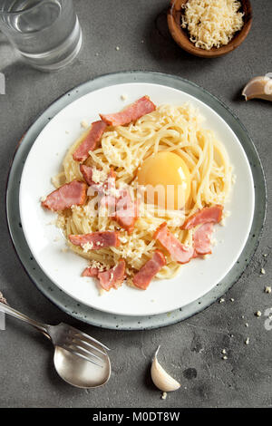 Spaghetti alla carbonara la pasta con la salsa di uova, pancetta e formaggio parmigiano grattugiato - le sane pasta italiana sul cemento grigio sfondo Foto Stock
