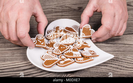 Mani femminili e il dolce gingerbreads per buona fortuna. I cookie decorativo e la piastra a forma di cuore su una tavola di legno. Amore, bond, matrimonio o amicizia. Foto Stock