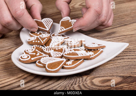 Mani femminili e dolce gingerbreads ornati per buona fortuna. San Valentino e biscotti a forma di cuore la piastra sulla tavola di legno. La cottura, feste e celebrazioni. Foto Stock