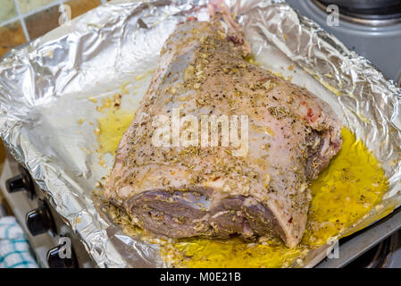 Closeup raw gamba di Agnello comune di torrefazione sul foglio di stagno con ingredienti pronti per la tostatura. Foto Stock