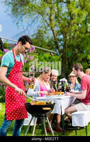 L'uomo cuocere carne sul giardino barbecue party Foto Stock