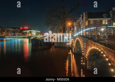 Amsterdam, Paesi Bassi, dicembre 16, 2017: Magere ponte sopra il fiume Amstel con sullo sfondo i canali caratteristici edifici in o Foto Stock