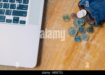 Laptop e molte monete di denaro nella borsa blu sulla tavola di legno Foto Stock