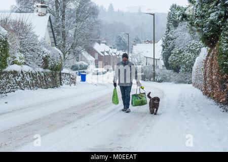 A Killearn, Stirlingshire, Scotland, Regno Unito - 21 Gennaio 2018: Regno Unito meteo - uomo a camminare con il cane di strada innevata con lo shopping forniture dal negozio del villaggio dopo la nevicata nel villaggio di Stirlingshire del credito a Killearn: Kay Roxby/Alamy Live News Foto Stock