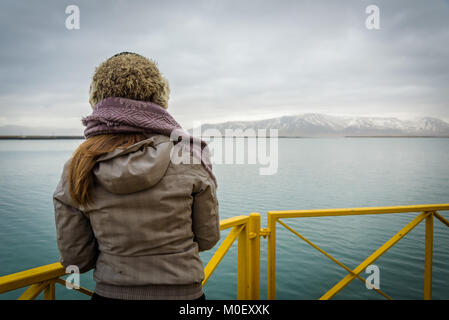 Donna che guarda il mare e le montagne nevose dal faro giallo a Reykjavik, Islanda. Foto Stock