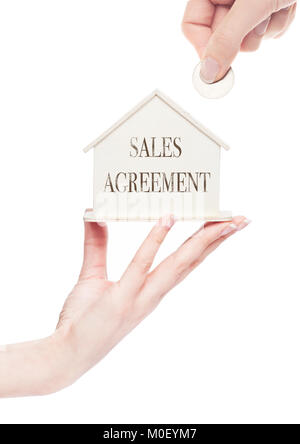 Femmina trattiene a mano in legno modello di casa e la mano che tiene la moneta con testo concettuale. Accordo di vendita Foto Stock